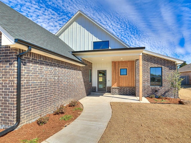 view of front of home with board and batten siding, brick siding, and a shingled roof