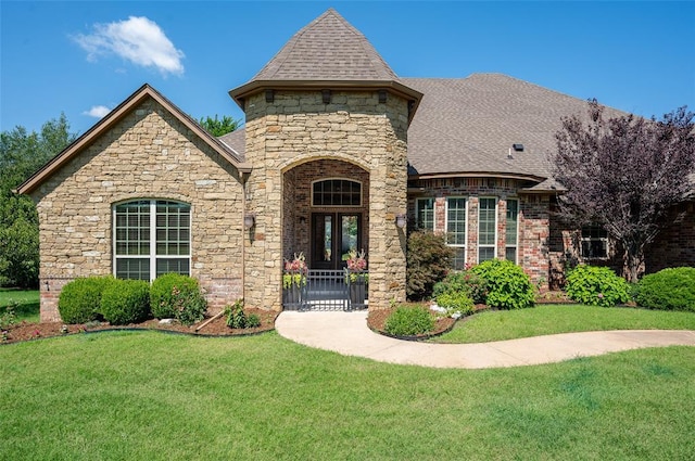 french provincial home with a shingled roof, a front yard, and brick siding