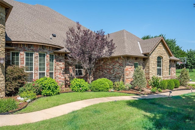 view of front of house featuring a shingled roof, brick siding, and a front lawn