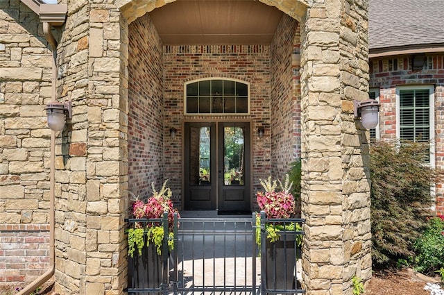 doorway to property with stone siding, roof with shingles, a gate, french doors, and brick siding