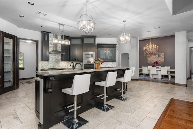 kitchen featuring stainless steel appliances, visible vents, wall chimney exhaust hood, tasteful backsplash, and glass insert cabinets