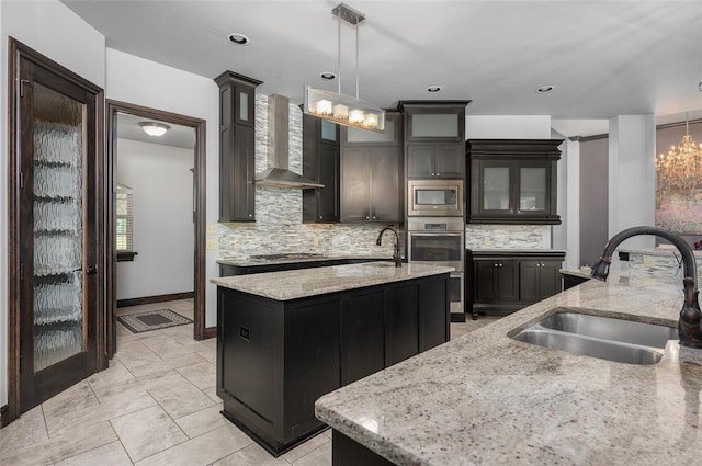 kitchen with tasteful backsplash, a center island with sink, appliances with stainless steel finishes, wall chimney range hood, and a sink