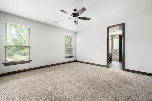 carpeted spare room featuring ceiling fan, a wealth of natural light, visible vents, and baseboards