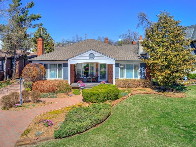 view of front of home featuring brick siding, roof with shingles, and a front lawn