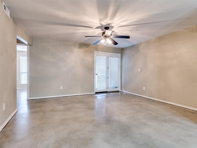 spare room featuring baseboards, concrete floors, visible vents, and a ceiling fan