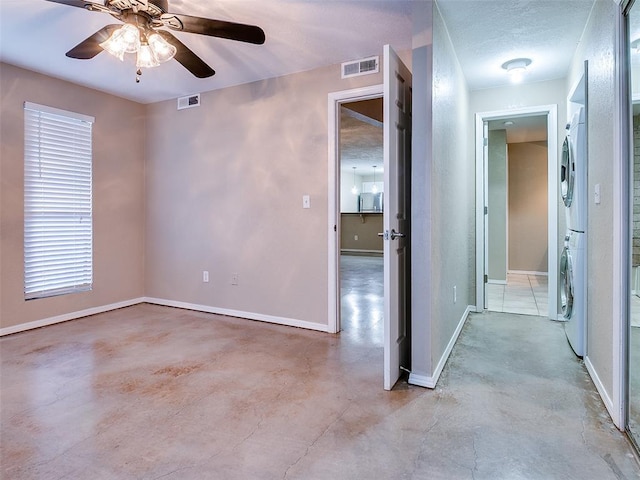 spare room with a ceiling fan, stacked washer / dryer, visible vents, and baseboards