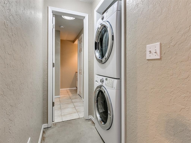 laundry room with laundry area, baseboards, a textured wall, and stacked washing maching and dryer