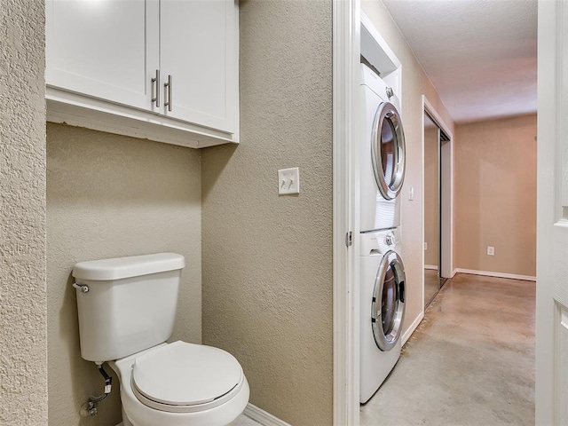 laundry area featuring a textured wall, laundry area, stacked washing maching and dryer, and baseboards