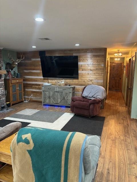 living area with recessed lighting, visible vents, wooden walls, and wood finished floors