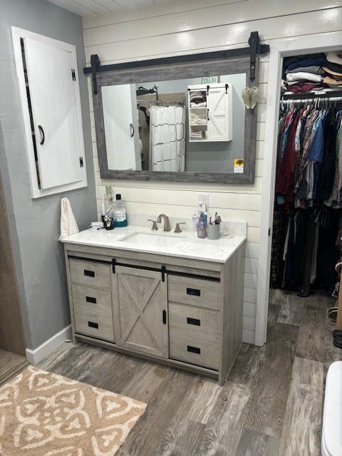 bathroom featuring vanity, a walk in closet, baseboards, and wood finished floors