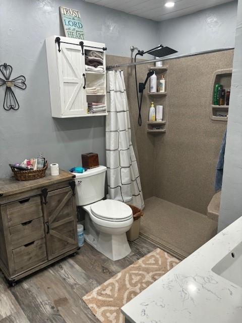 bathroom with vanity, toilet, wood finished floors, and tiled shower