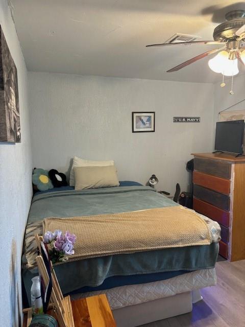 bedroom with ceiling fan, visible vents, and wood finished floors