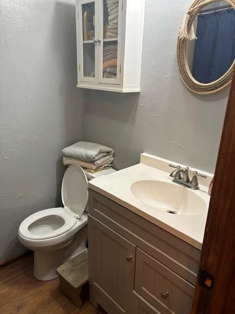 half bathroom featuring vanity, toilet, wood finished floors, and a textured wall