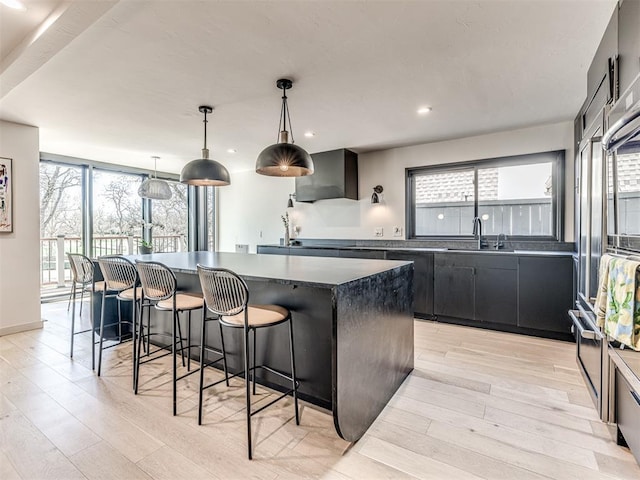 kitchen with light wood-type flooring, a sink, dark countertops, a center island, and dark cabinets