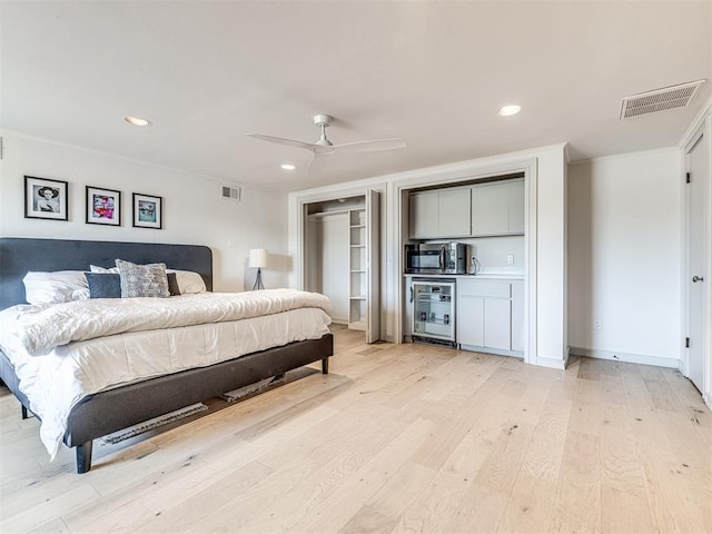 bedroom featuring beverage cooler, visible vents, light wood-style flooring, and ornamental molding