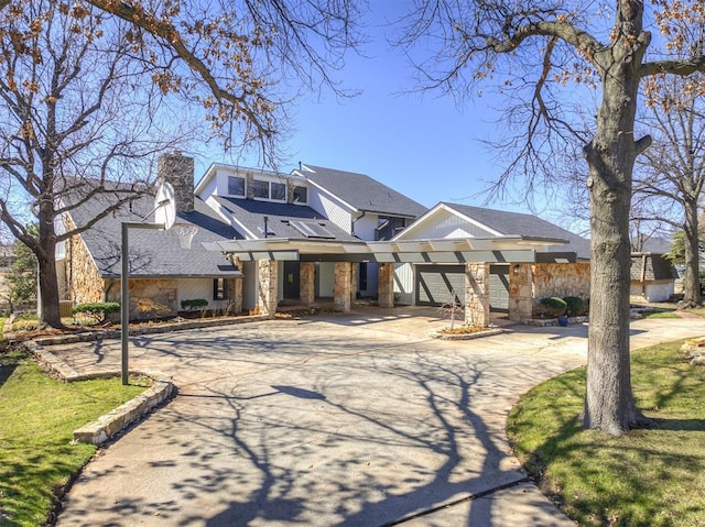 view of front of house featuring a chimney, concrete driveway, a front lawn, a garage, and stone siding