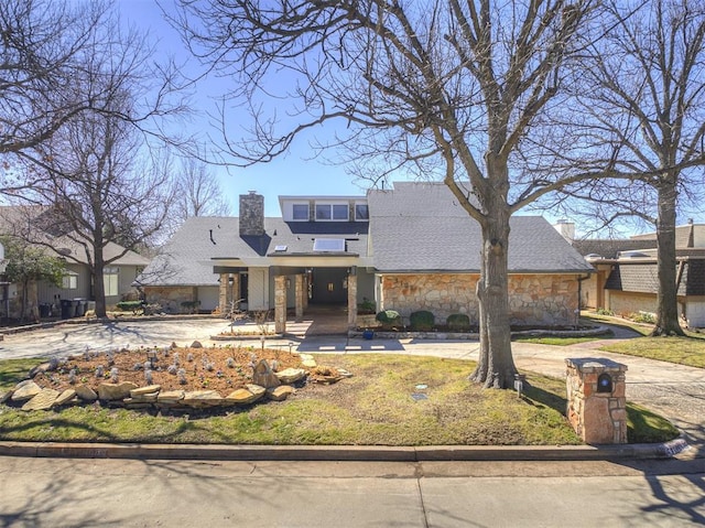 view of front facade with stone siding, driveway, and a chimney