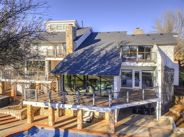 back of house with a shingled roof, a balcony, an outdoor pool, and a chimney