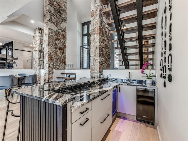 kitchen with visible vents, light wood finished floors, dark stone counters, a peninsula, and white cabinetry