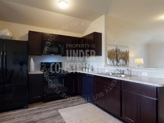 kitchen with lofted ceiling, a peninsula, light countertops, black appliances, and a sink