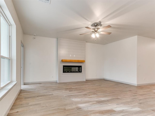 unfurnished living room featuring light wood-type flooring, a large fireplace, ceiling fan, and baseboards