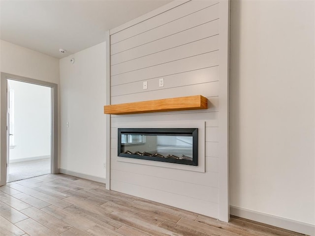 unfurnished living room featuring a large fireplace, baseboards, and light wood finished floors