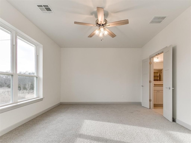 spare room featuring light carpet, ceiling fan, visible vents, and baseboards