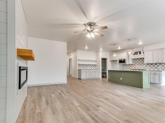 kitchen featuring light wood-style floors, stainless steel microwave, a ceiling fan, and decorative backsplash