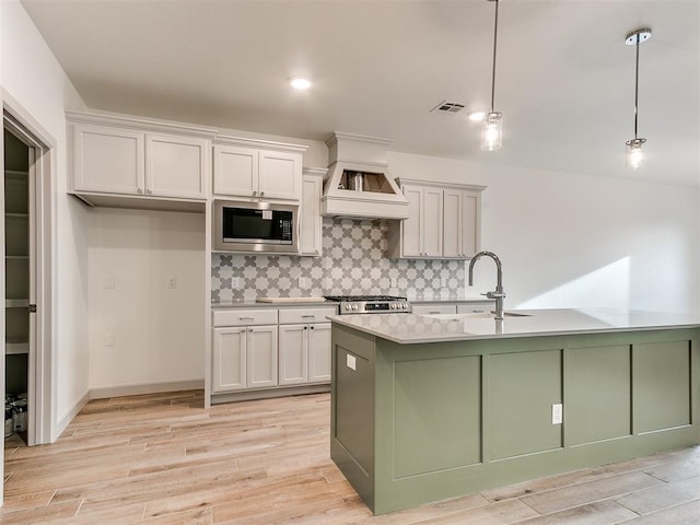 kitchen featuring tasteful backsplash, stainless steel microwave, visible vents, light wood-style floors, and a sink