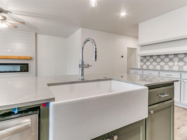 kitchen with light wood-style flooring, a sink, white cabinets, stainless steel dishwasher, and decorative backsplash