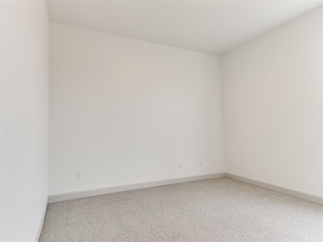 spare room featuring light carpet and baseboards