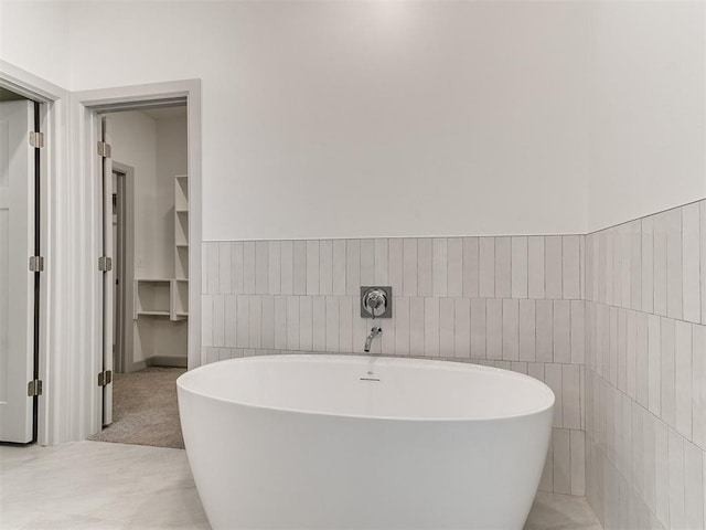 full bath featuring a soaking tub, tile walls, and wainscoting