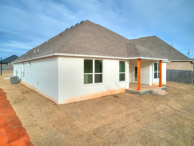 rear view of house featuring roof with shingles, fence, brick siding, and central AC unit