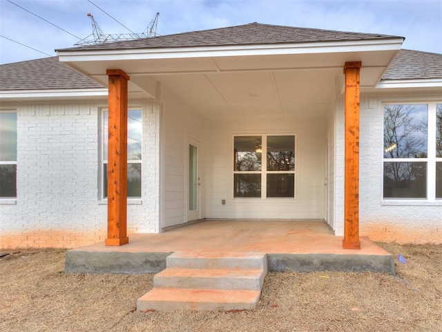 entrance to property featuring brick siding and roof with shingles