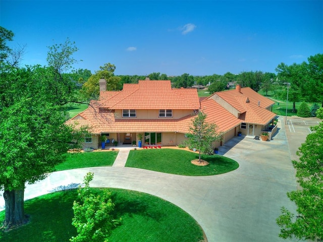 view of front of house with driveway, a tile roof, a chimney, and a front lawn