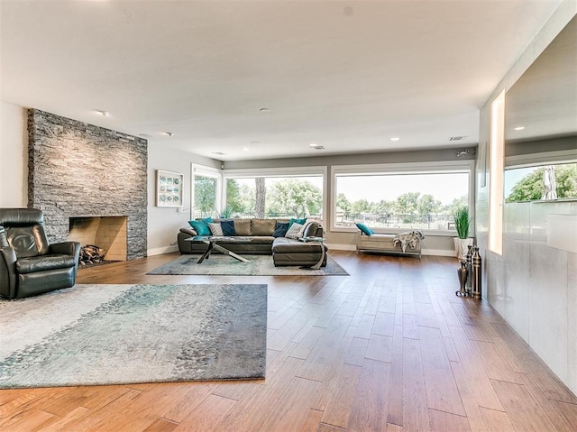 living room featuring a stone fireplace, wood finished floors, and a healthy amount of sunlight