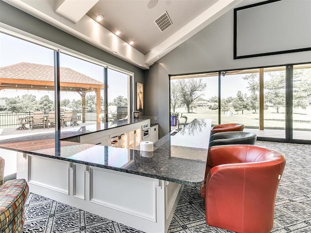 interior space featuring vaulted ceiling, dark stone counters, visible vents, and white cabinets