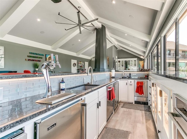 kitchen featuring tasteful backsplash, lofted ceiling with beams, white cabinets, a sink, and dishwasher