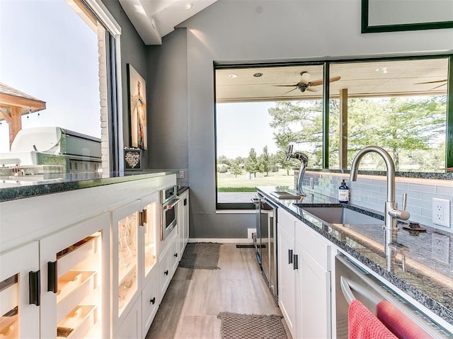 kitchen featuring stainless steel dishwasher, dark stone countertops, a sink, and white cabinetry