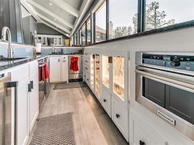 kitchen featuring backsplash, white cabinetry, a sink, oven, and beamed ceiling