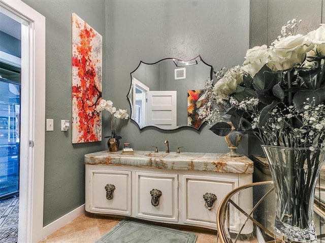 bathroom featuring a textured wall, vanity, visible vents, baseboards, and tile patterned floors