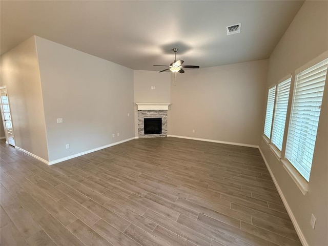 unfurnished living room featuring visible vents, a ceiling fan, a stone fireplace, wood finished floors, and baseboards