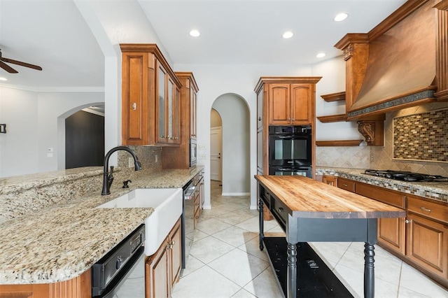 kitchen with arched walkways, appliances with stainless steel finishes, custom exhaust hood, wooden counters, and a sink