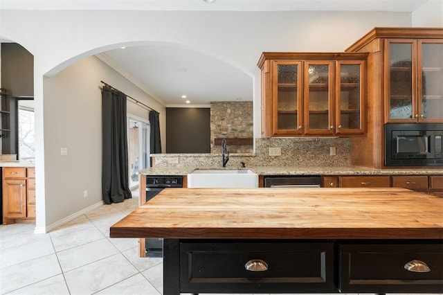 kitchen featuring black microwave, arched walkways, light tile patterned flooring, a sink, and backsplash