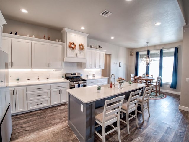 kitchen featuring visible vents, gas range, decorative backsplash, and white cabinetry