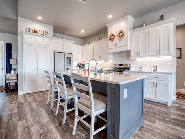 kitchen featuring wood finished floors, a center island with sink, stainless steel range with gas stovetop, freestanding refrigerator, and white cabinets