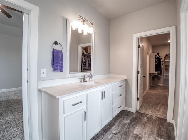 bathroom with a walk in closet, wood finished floors, vanity, and ceiling fan