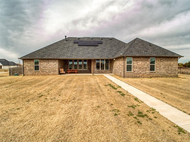 back of house featuring roof mounted solar panels, a patio, a yard, a shingled roof, and brick siding