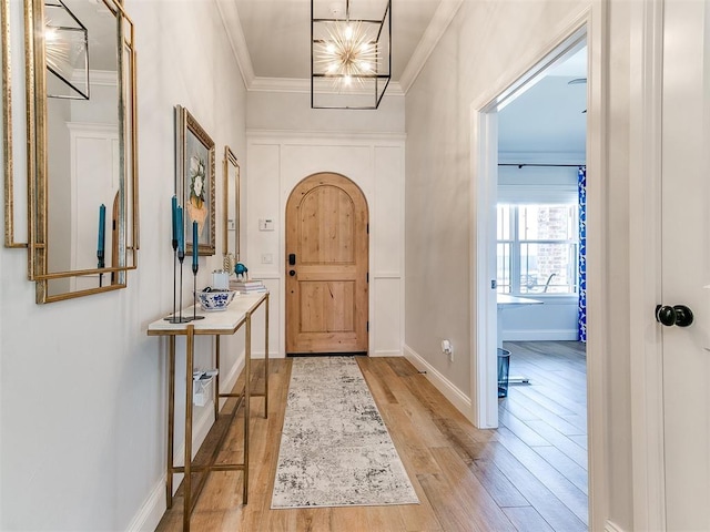 entrance foyer with arched walkways, wood finished floors, baseboards, ornamental molding, and an inviting chandelier