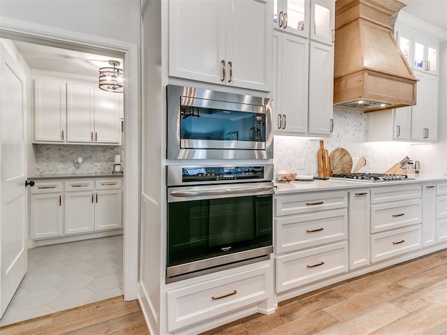 kitchen featuring stainless steel appliances, light wood-style floors, white cabinets, light countertops, and custom exhaust hood